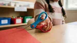 Close-up of a child’s hand demonstrating the correct ergonomic grip on safety scissors for kindergarten arts and crafts.